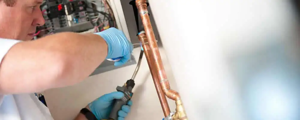 Water heater repair technician testing copper pipe connections and controls in Aurora, CO